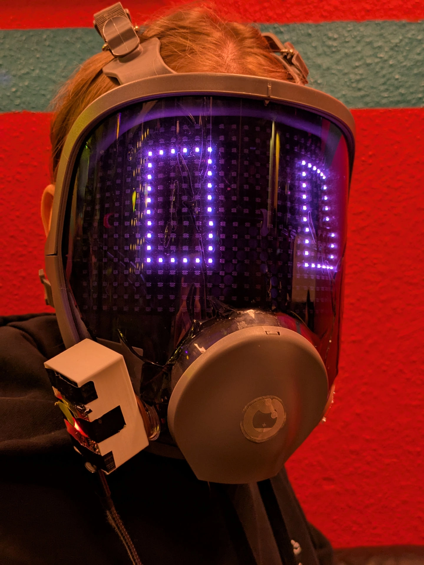 beeper with a visor on with some prototype casing for the micro controller attached to the filter port. faceplate showing 2 purple glowing boxes