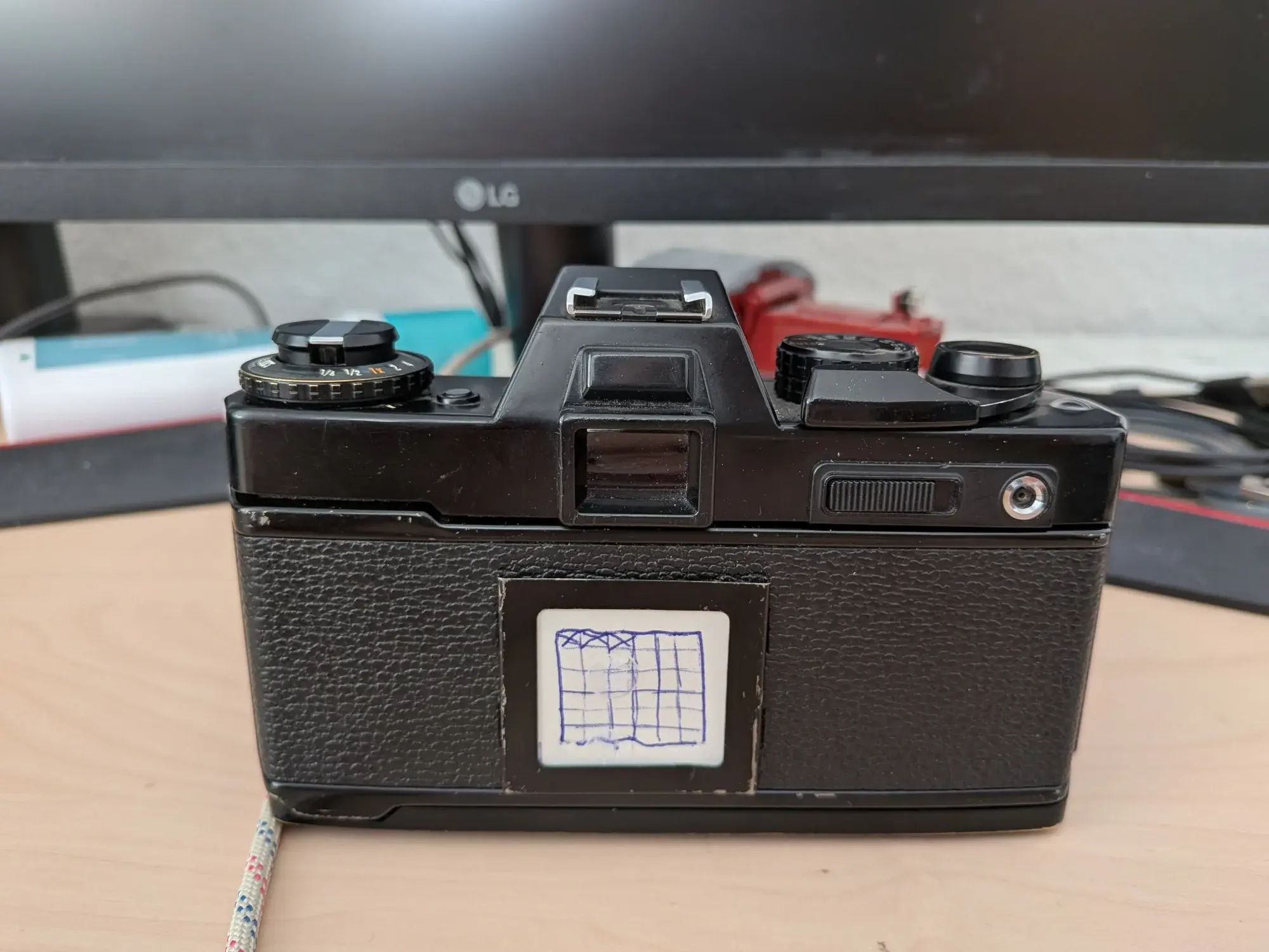 A Yashica FR-1 sitting on a table
a small white peice of cardboard is in the thingy that usually holds the info about what film is loaded with a 6x6 grid squiggly drawn with a pen on it
3 boxes are already checked